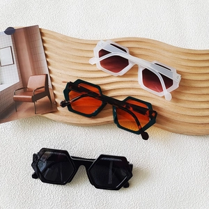 Three pairs of geometric hexagonal sunglasses in white, green, and black on a wooden stand