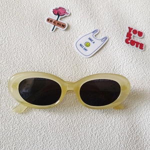 Nahaufnahme der Retro-Oval-Sonnenbrille mit cremegelbem Rahmen und dunklen Gläsern auf Weiß