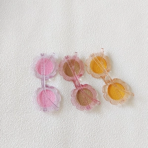 Flat lay of three sunflower-shaped children's sunglasses in pink, brown and orange