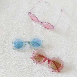 Flat lay of flower-shaped children's sunglasses with glitter resin frames in three colors