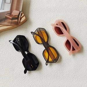 Three retro hexagonal thick frame sunglasses in black, tea, and pink displayed on a textured surface