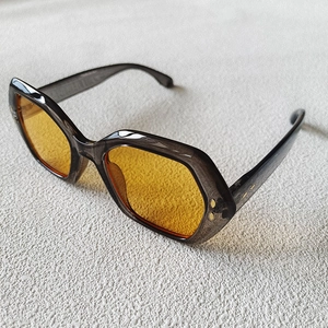 Detail of oversized irregular sunglasses with grey transparent frame and yellow lenses