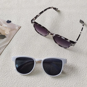 Flat lay of champagne and white square sunglasses with gold metal hinge details