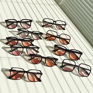 Flat lay of multiple black frame sunglasses with pink gradient lenses under natural shadows
