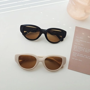 Flat lay of futuristic cat-eye sunglasses in black and beige with dark brown lenses