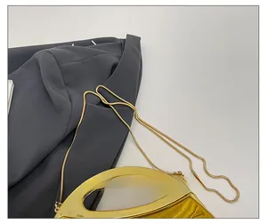 Detail der goldenen Acryl-Clutch mit schlangenförmiger Metallkette und ausgeschnittenem Griff