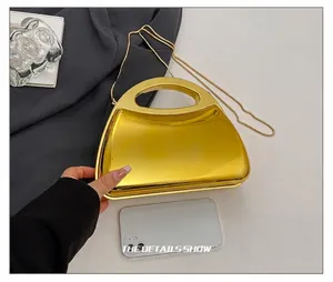 Detail of mirror gold acrylic evening bag showing the handle and metallic chain strap