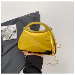 Detail einer goldenen Acryl-Box-Tasche mit Spiegelglanz, Rundgriff und einer Metallkette
