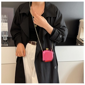 Detail of a bright pink geometric acrylic mirror clutch bag with a gold chain strap