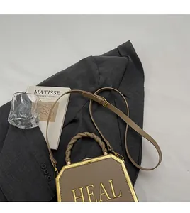 Detail of khaki octagonal handbag with gold HEAL lettering and woven handle on a suit