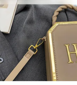 Detailed close-up of golden metal hook and leather strap on khaki box handbag