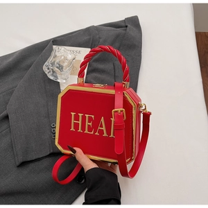 Detail of red leather box bag featuring golden HEAR lettering and twisted handle