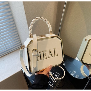 Detail view of white octagonal handbag with golden HEAL logo and twisted rope handle