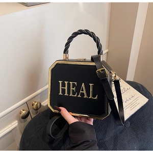 Detailed macro view of black box bag featuring bold gold 3D HEAL metal lettering