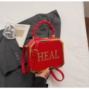 Detail of red leather octagon handbag with gold HEAL logo on a gray suit background
