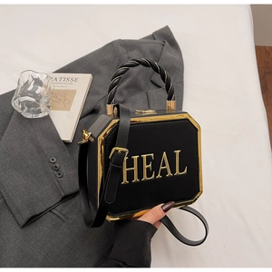 Detail of black box bag with gold HEAL letters and top handle on a gray blazer