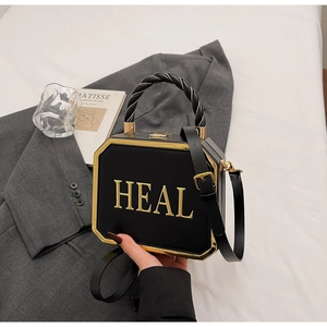 Detail of octagonal black box bag with golden HEAL lettering and woven rope handle