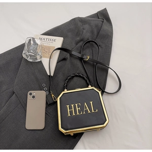 Detail of black octagonal box bag featuring golden HEAL lettering and braided handle