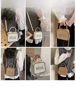 Detail of a rigid box crossbody bag with metal edges and HEAL lettering in cream color