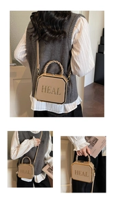 Detail showing khaki box bag with gold HEAL letters, woven handle and contrast edges