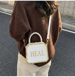 White octagonal crossbody box bag with gold metal trim and HEAL lettering detail