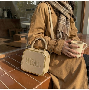 Detail of octagonal beige crossbody bag with gold HEAL lettering and braided handle