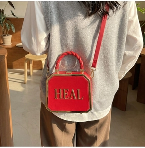 Detail of red octagonal crossbody bag with golden HEAL lettering and woven handle