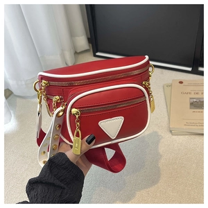 Détail du sac ceinture en cuir rouge et blanc avec boucles dorées et rivets sur la bandoulière