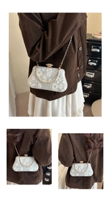 Lace evening bag detail showing white floral patterns, gold ring handle and pearl clasp