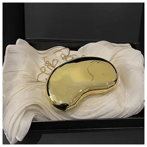 Detailed close-up of a golden bean-shaped acrylic clutch with a metallic chain on silk
