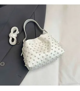 Dettaglio borsa a secchiello bianca con perle e tracolla in PU su sfondo di blazer grigio