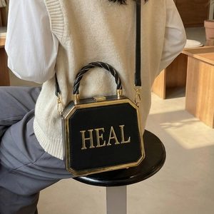 Octagonal black leather handbag with gold HEAL letters and twist handle on a female model