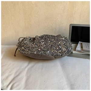 Detail of silver sequin drawstring handbag with textured suede base on a desk