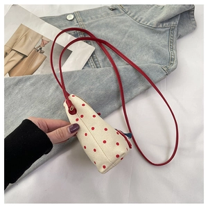 Close-up of cream canvas crossbody bag with red polka dots and matching thin strap
