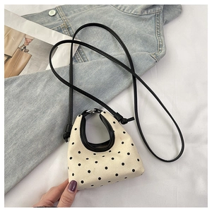 Detailed shot of beige polka dot canvas mini handbag with thin black shoulder strap