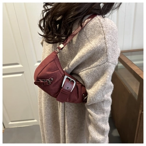 Detail of burgundy retro motorcycle underarm bag with silver buckles on beige sweater