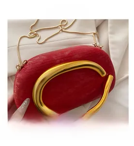 Macro shot of red clutch featuring a large gold C-shaped metal handle and gold chain