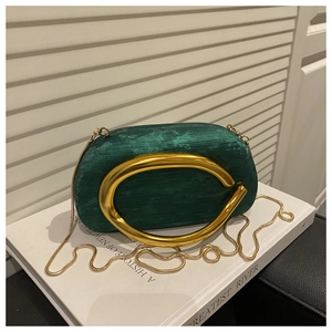 Detail of emerald velvet clutch bag with gold C-shaped metal handle and chain strap