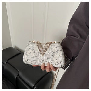 Detail of white lace evening bag with rhinestones and gold V-shaped metal buckle clasp