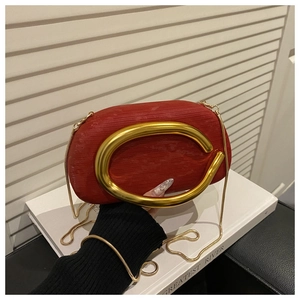 Detail of red textured clutch bag featuring a prominent gold C-shaped buckle and chain
