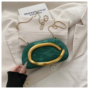 Macro detail of dark green clutch bag featuring a large golden C-ring and snake chain