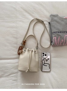 Close-up of cream bucket bag with lychee texture and striped bear pendant detail