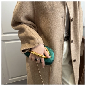 Close-up of green velvet evening clutch with artistic gold handle and chain strap detail