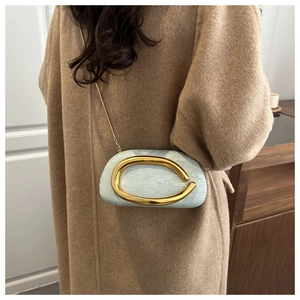 Blue box clutch featuring a large gold metal handle and chain strap shown on a camel coat