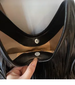 Detail of magnetic snap closure and fringe tassels on black leather bucket shoulder bag