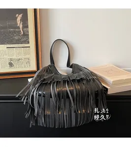 Detail of black leather handbag featuring long tassels and a sturdy curved handle