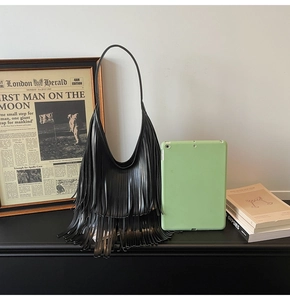 Detail of a black crescent shoulder bag featuring long fringe layers and a wide strap