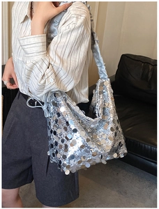 Detail of silver sequined hobo bag with ruffled shoulder strap worn in indoor setting