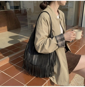 Detail of a large black leather hobo bucket bag with stylish long fringes and shoulder strap
