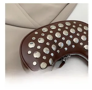 Detail of silver rivets and metal zipper on a dark brown leather crescent saddle bag
